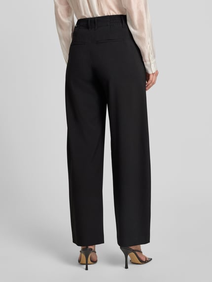 Vrouwenmodel draagt zwarte wide fit dames stoffen broek van Drykorn model 'Dutiful', elastische materiaalmix met viscose, achterzakken, haakjes- en ritssluiting, bandwijdte maat 27/32: 36 cm, binnenbeenlengte 78 cm. Ganzlichamige achteraanzicht.