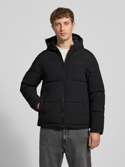 Männermodel trägt schwarze Steppjacke mit Kapuze Modell 'GALAXY' von JACK & JONES, gerade Passform, Reißverschluss, Eingrifftaschen, Ganzkörperansicht von vorne.