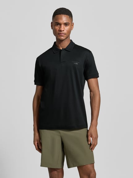 Männermodel trägt Regular Fit Poloshirt aus reiner Baumwolle Modell 'PS Spirit 70 Plk' von BOSS Green X PORSCHE, unifarben, Kurzarm, Ganzkörperansicht von vorne.