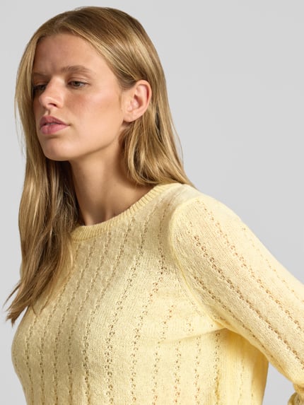 Frauenmodel trägt Regular Fit Pullover mit gerippten Ärmelbündchen Modell 'ADA' von PIECES in zartem Gelb, leichte Strickstruktur, Nahaufnahme Oberkörper.