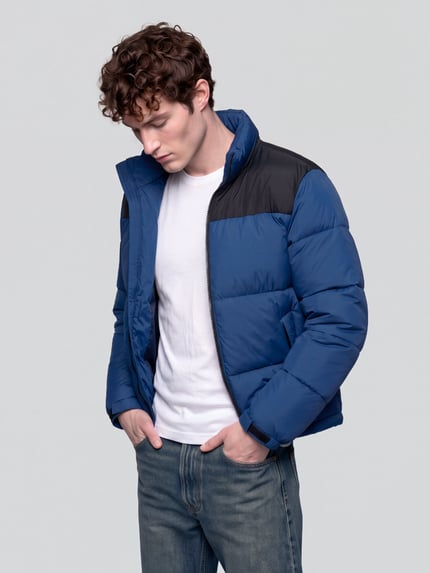 Männermodel trägt Steppjacke mit hohem Stehkragen Modell 'ONSMAVERICK' von ONLY in Blau mit schwarzen Details, unifarben, Regular Fit, cropped, Label-Detail, Reißverschlusstaschen, elastische Abschlüsse, Kragen, Reißverschluss, langarm, Ganzkörperansicht von vorne.