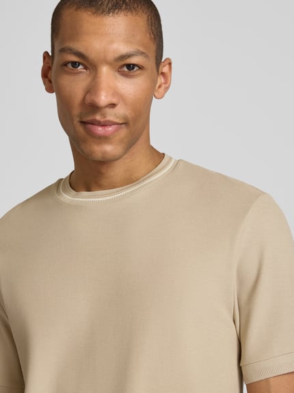 Männermodel trägt Regular Fit T-Shirt aus reiner Baumwolle Modell 'C-TAUT-40' von BOSS in Beige, Piqué-Struktur, Nahaufnahme Oberkörper.