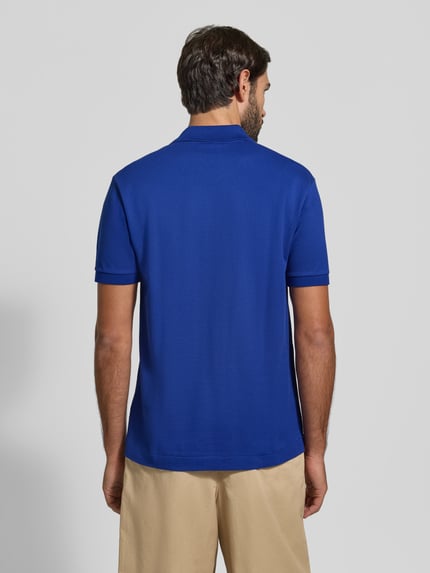 Männermodel trägt Regular Fit Poloshirt aus reiner Baumwolle von Lacoste in kräftigem Blau, beige Hose, Ganzkörperansicht Rückansicht, Herren Poloshirt von Lacoste.