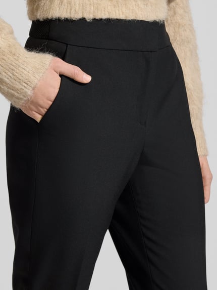 Vrouwenmodel draagt Regular Fit Schmale Hose mit Bügelfalten van s.Oliver BLACK LABEL, effen zwart, persplooien, zij-steekzakken, mid waist, labelstitching, elastische band met structuur, schiebehaken en verborgen ritssluiting, elastische boord, detailopname heup.