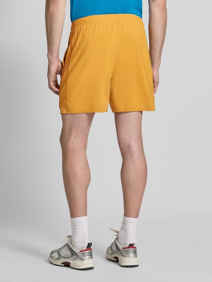 Männermodel trägt Regular Fit Shorts mit integriertem Slip Modell 'Core' von ASICS TIGER in Gelb, elastischer Bund, Ganzkörperansicht Rückansicht. Kontext: Herren Shorts, integrierter Slip, Logo-Print, Bundweite 38 cm (Größe M), Innenbeinlänge 17 cm (Größe M).
