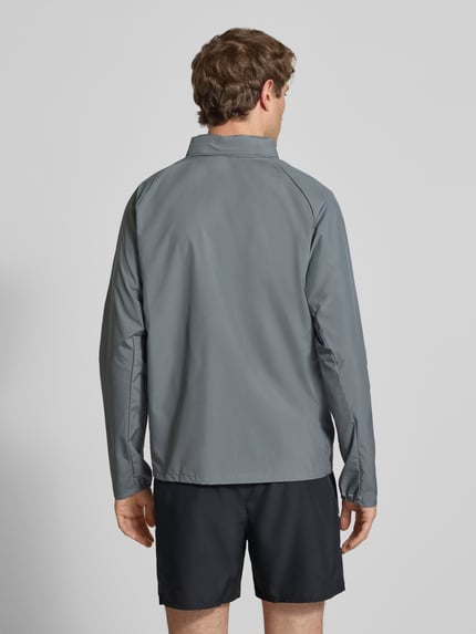 Männermodel trägt Regular Fit Jacke mit Stehkragen Modell 'Miler' von NIKE TRAINING in Grau mit Logo-Print, Ganzkörperansicht Rückansicht.