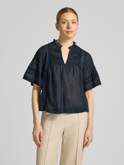 Frauenmodel trägt Blusenshirt mit V-Ausschnitt Modell 'Siama' von Neo Noir, Regular-Fit, Stitchings, dunkelblau, luftige Textur, Ganzkörperansicht von vorne. Rückenlänge bei Größe 36: 56 cm, Ärmellänge bei Größe 36: 28 cm.