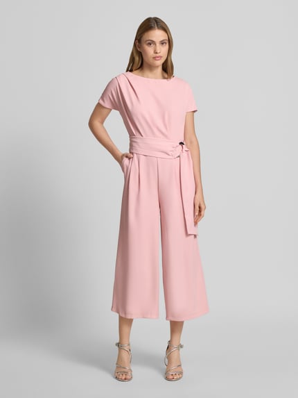 Modelka kobieca nosi Jumpsuit mit Stretch-Anteil od Betty Barclay w kolorze pudrowego różu, krój regular fit, długość 7/8, pasek w talii, krótkie rękawy, okrągły dekolt, z przodu zakładki, tekstura gładka, widok całej sylwetki z przodu, Szerokość w rozmiarze 36: 37 cm, długość tyłu: 38 cm, długość całkowita: 127 cm, długość rękawa: 23 cm, długość nogawki wewnętrznej: 58 cm.