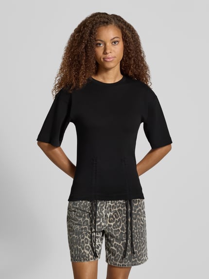 Modelka prezentuje damski t-shirt z bawełny, prosty krój, model 'MALLE' od Topshop, okrągły dekolt, marszczenia z wiązaniem, długość tyłu 66 cm w rozmiarze S, ciemny kolor, gładka faktura, całkowity widok z przodu.