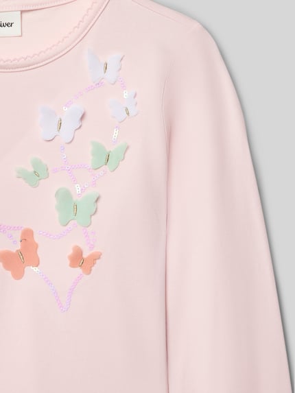 Mädchen trägt Regular Fit Langarmshirt aus Baumwoll-Mix von s.Oliver RED LABEL, pastellrosa, Schmetterlings-Applikation, Effektgarn, Nahaufnahme Oberkörper.