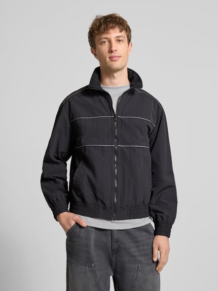 Mężczyznamodel nosi Regular Fit Blouson mit Kontraststreifen Modell 'HEIGHTS PIPPING JACKET' od Levi's®, czarna kurtka z kontrastowymi paskami, stójka, suwak, boczne kieszenie, dzianinowe ściągacze, gładka tekstura, całkowity widok z przodu