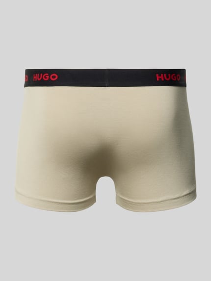 Männermodel trägt Trunk aus Baumwoll-Mix im 3er-Pack von HUGO für Herren in Beige mit schwarzem Bund und rotem Logo, Ganzkörperansicht Rückansicht.