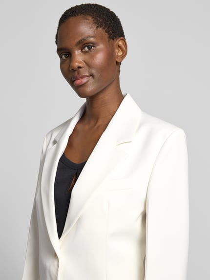Modelka kobieca ma na sobie Blazer aus Woll-Mix mit Brusttasche od Victoria Beckham, biały, krój slim fit, kieszeń na piersi, nałożone kieszenie, zapięcie na dwa guziki, długość tyłu w rozmiarze 36: 73 cm, szerokość w rozmiarze 36: 46 cm, długość rękawa w rozmiarze 36: 63 cm, gładka tekstura, prosty krój, zbliżenie na górną część ciała