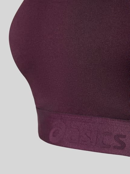 Frauenmodel trägt Sport-BH mit Racerback Modell 'ROAD COMPRESSION' von ASICS in dunkellila, Logo-Saum, Material-Mix, Nahaufnahme Oberkörper.