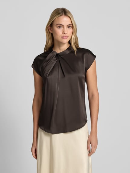 Kobiece modelka nosi Blusentop aus Satin mit Knotendetail Modell 'Fleur Drapy' od Neo Noir, satyna, krój regular fit, długość tyłu w rozmiarze 36: 59 cm, widok całej sylwetki z przodu.