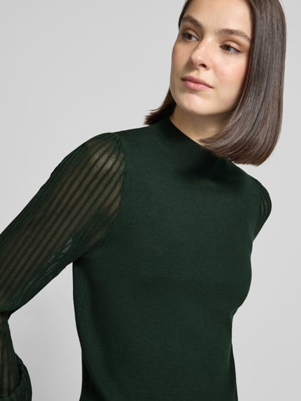 Frauenmodel trägt Strickpullover aus Viskose-Mix mit Stehkragen von zero, semitransparente Ärmel in Ripp-Optik, Nahaufnahme Oberkörper.