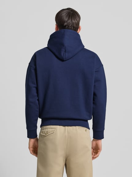 Männermodel trägt Relaxed Fit Hoodie mit Label-Stitching und Känguru-Tasche von Polo Ralph Lauren im Baumwoll-Mix, Ganzkörperansicht Rückansicht. Herren Hoodie, Rückenlänge 67 cm, Ärmellänge 54 cm, dunkelblau-beige Farbkombination, strukturierte Oberfläche.