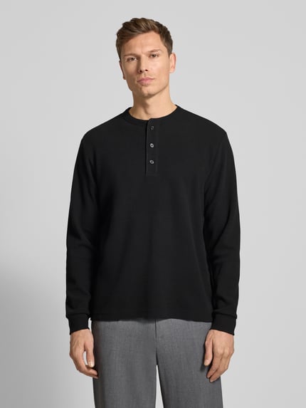 Männermodel trägt Regular Fit Pullover mit Knopfleiste Modell 'Kilano' von Drykorn, Baumwoll-Mix, schwarzes Strukturmuster, Ganzkörperansicht von vorne.