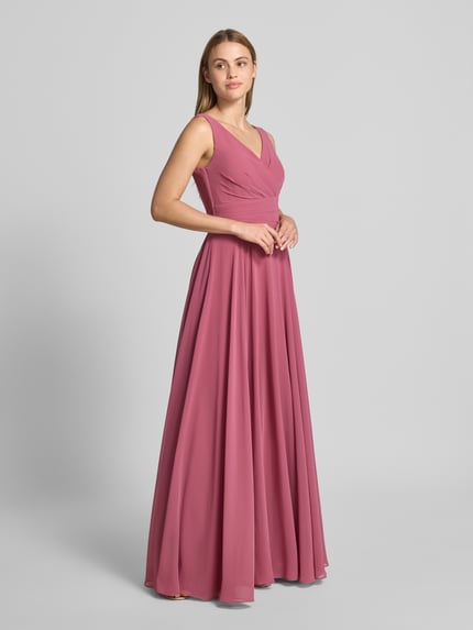 Frauenmodel trägt Maxikleid aus Chiffon in Wickel-Optik von TROYDEN COLLECTION in A-Linie, mattes Rosa, fließende Textur, Ganzkörperansicht von vorne.
