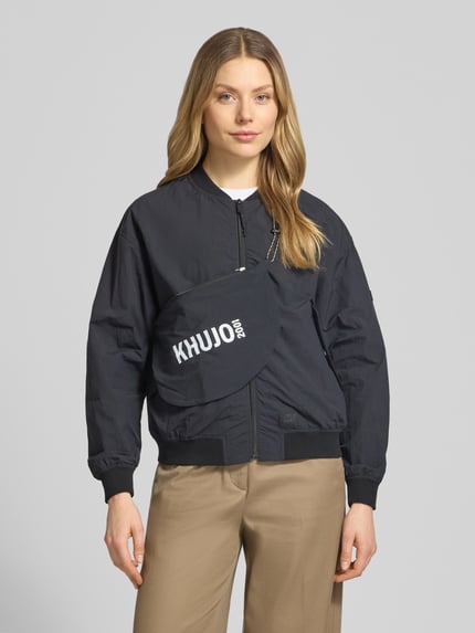 Frauenmodel trägt Jacke mit Pattentaschen Modell 'FACEE' von khujo in Schwarz, Regular-Fit, Stehkragen, Reißverschluss, Umhängetasche, Nahaufnahme Oberkörper. Rückenlänge bei Größe S: 60 cm, Schulterbreite: 50 cm, Brustweite: 55 cm, Ärmellänge: 56 cm.