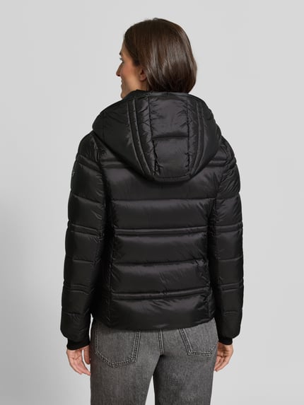 Vrouwenmodel draagt Steppjacke met Kapuze en Reißverschlusstaschen van MICHAEL Michael Kors in zwart, doorgestikte naden, recht model, Ganzkörperansicht Rückansicht. Ruglengte maat S: 63 cm, schouderbreedte 43 cm, borstwijdte 53 cm, mouwlengte 68 cm.