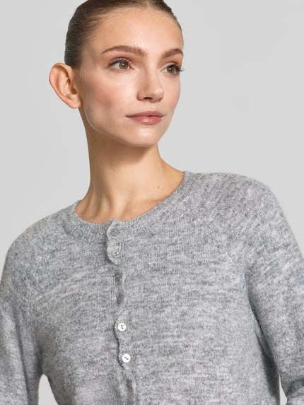 Frauenmodel trägt Regular Fit Strickjacke aus Woll-Mix Modell 'SAGE' von ICHI, hellgrau meliert, gerippte Abschlüsse, Nahaufnahme Oberkörper. Damen Strickjacke elastischer Woll-Mix mit Alpaka-Anteil, durchgängige Knopfleiste, langärmlig, Rückenlänge 52 cm, Ärmellänge 70 cm.