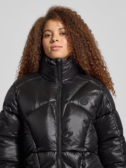 Frauenmodel trägt Oversized Steppjacke Modell 'FRESIA-1' von Hugo Blue, Optik: Unifarben, Stehkragen, Logo-Patch, wasserabweisend, Nahaufnahme Oberkörper.
