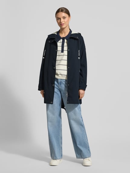 Modelka nosi Jacke mit Ärmelriegeln od NAUTGÅRD, kolor granatowy, krój regular fit, kaptur z tunelem, listwa guzikowa, kieszenie zapinane na zamek błyskawiczny, patki przy mankietach, długość tyłu 90 cm, szerokość ramion w rozmiarze S: 45 cm, szerokość klatki piersiowej w rozmiarze S: 51 cm, długość rękawów w rozmiarze S: 62 cm, widok całej sylwetki od przodu.