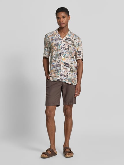Mannelijk model draagt Relaxed Fit Freizeithemd aus Viskose mit Reverskragen van Lindbergh in all-over print, bruin-beige tinten, luchtige stof, korte mouwen, geheel vooraanzicht, context: herenoverhemd van pure viscose, relaxed fit, reverskraag, ruglengte maat M 74 cm, schouderbreedte maat M 50 cm, mouwlengte maat M 32 cm.