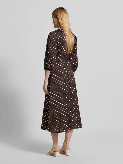 Frauenmodel trägt Regular Fit Maxikleid mit V-Ausschnitt von Neo Noir aus braunem Satin mit weißen Punkten, 3/4-Arm, Wickel-Optik, elastische Ärmelabschlüsse, Raffungen, Ganzkörperansicht Rückansicht.