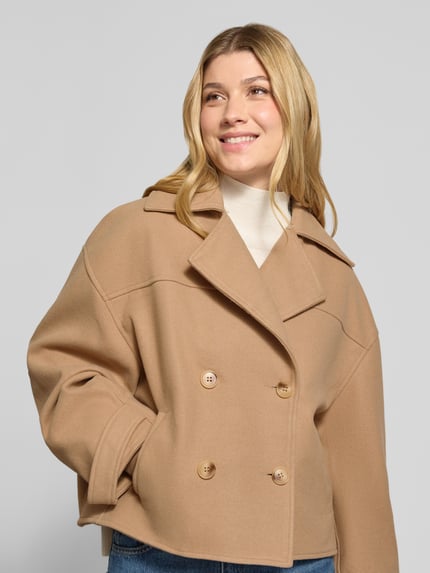 Modelka nosi Straight Fit Jacke mit doppelreihiger Knopfleiste von monari, beżowy kolor, Mieszanka materiałów z dodatkiem wiskozy, Kołnierz z połami, wpuszczane kieszenie, regulowane patki przy mankietach, długość tyłu w rozmiarze 36: 57 cm, szerokość ramion w rozmiarze 36: 61 cm, szerokość w rozmiarze 36: 56 cm, długość rękawów w rozmiarze 36: 51 cm, tekstura gładka, widoczne dwurzędowe guziki, widok całej sylwetki z przodu.