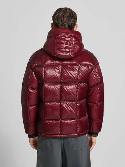 Männermodel trägt Steppjacke mit Zweiwege-Reißverschluss von Armani Exchange in glänzendem Dunkelrot, wattierte Textur, Ganzkörperansicht Rückansicht. Rückenlänge, Schulterbreite, Brustweite und Ärmellänge passend für Größe M, Slim Fit, Kapuze mit Tunnelzug, Label-Detail.