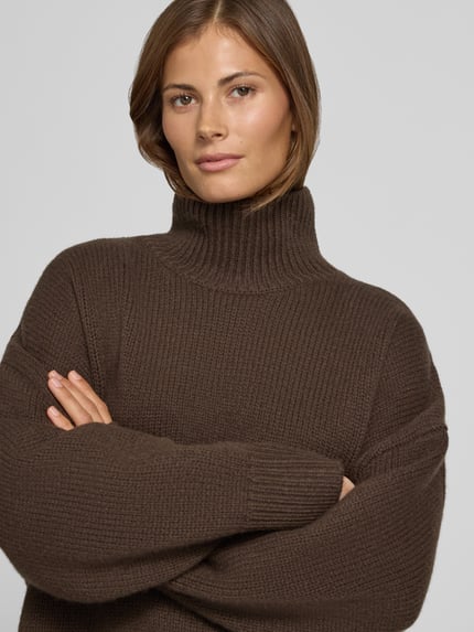 Frauenmodel trägt Wollpullover mit Rollkragen von Style Icon Collection in Dunkelbraun, reine Wolle, lockerer Schnitt, gerippte Abschlüsse, Nahaufnahme Oberkörper.