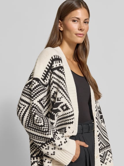 Frauenmodel trägt Oversized Strickjacke aus reiner Wolle Modell 'BELGIO' von Max Mara im Weekend Max Mara Kontext, cremefarben mit schwarzem Muster, weiche Stricktextur, Nahaufnahme Oberkörper.