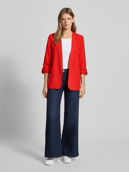 Frauenmodel trägt Regular Fit Longblazer mit Viskose-Anteil Modell 'BOSELLA' von Pieces, Optik: Unifarben, Reverskragen, Schulterpolster, 3/4-Arm, Ärmelabschluss gerafft, Materialverarbeitung: Webstruktur, leuchtendes Rot, mit weißem Oberteil und dunkelblauer weiter Jeans, Ganzkörperansicht von vorne.