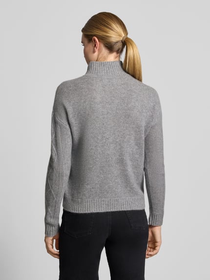 Vrouwenmodel draagt pullover van kasjmier met kabelpatroon van Christian Berg Woman in lichtgrijs, recht model, opstaande kraag, ribboorden, ruglengte maat S 57 cm, mouwlengte maat S 64 cm, geheelbeeld achteraan.