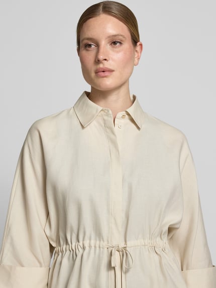 Frauenmodel trägt Relaxed Fit Bluse aus Lyocell-Mix mit 3/4-Arm von Comma, Hemdblusenkragen, Tunnelzug, glatter beigefarbener Stoff, Nahaufnahme Oberkörper.