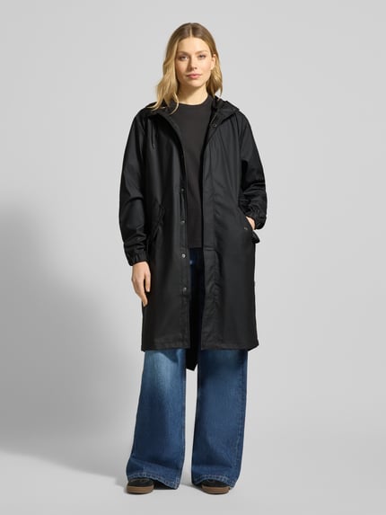 Frauenmodel trägt Regular Fit Parker mit Kapuze Modell 'Fishtail' von Rains, schwarze Farbe, Pattentaschen, elastische Ärmelabschlüsse, Ganzkörperansicht von vorne, Rückenlänge bei Größe S 104 cm, Schulterbreite 45 cm, Brustweite 55 cm, Ärmellänge 65 cm.