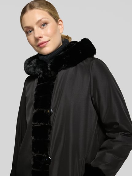 Frauenmodel trägt Regular Fit Mantel mit Wendefunktion und Webpelz-Innenseite von PETITE M., Farbe Schwarz, Nahaufnahme Oberkörper, Knopfleiste und Eingrifftaschen, Rückenlänge 85 cm, Schulterbreite 39 cm, Brustweite 50 cm, Ärmellänge 62 cm.