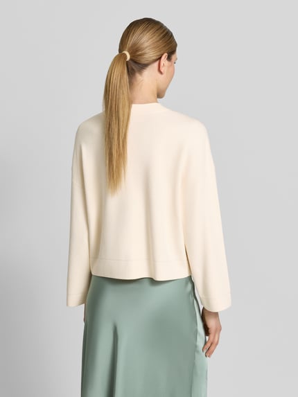 Frauenmodel trägt Strickjacke aus Viskose-Mix mit V-Ausschnitt von comma in offwhite, Relaxed Fit, glatte Textur, Rückansicht, Ganzkörperansicht.