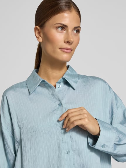 Frauenmodel trägt Longline Langarmbluse mit Crinkle-Struktur von OPUS in matt glänzendem, hellblau gestreiftem Webstoff, Nahaufnahme Oberkörper.