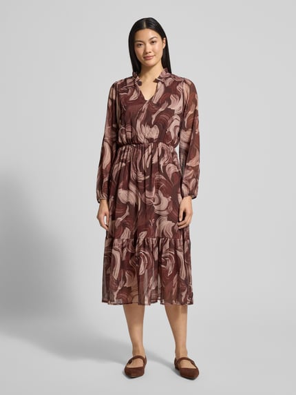 Modelka kobieca nosi Midikleid mit V-Ausschnitt Modell 'Za44raa' od ZABAIONE, wzór w liście, odcienie brązu, długość midi, A-linia, widok całej sylwetki z przodu.