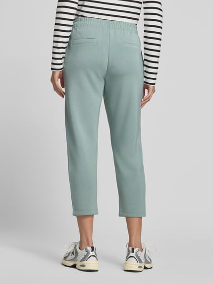 Frauenmodel trägt Cropped Sweatpants mit elastischem Bund und Eingrifftaschen von Christian Berg Woman, grüner Farbton, Material-Mix mit Modal-Anteil, Cropped, Ganzkörperansicht Rückansicht.