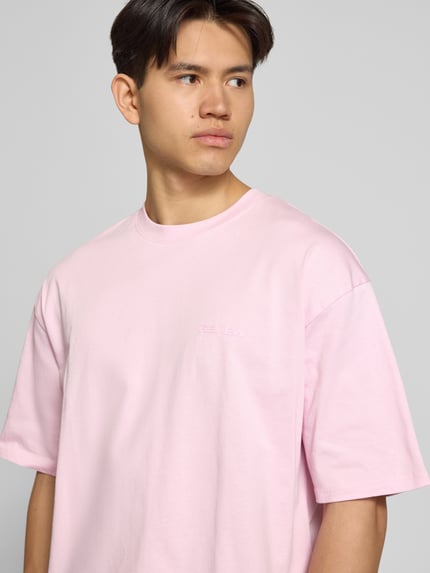 Männermodel draagt Oversized T-shirt met logo en ronde hals van REVIEW, puur katoen, oversized, logoprint, ruglengte maat M 68 cm, Nahaufnahme Oberkörper.