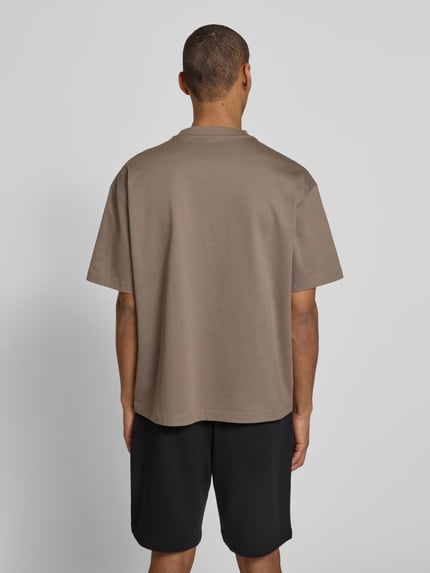 Männermodel trägt Relaxed Fit T-Shirt aus reiner Baumwolle Modell 'DINKEE' von HUGO in Uni-Optik mit 3D Label Print, Jersey, Rundhals, kurzarm, Ganzkörperansicht Rückansicht