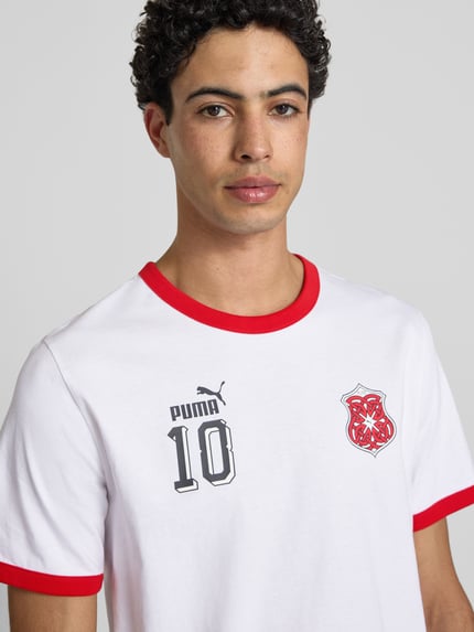 Männermodel trägt T-Shirt aus Baumwolle Modell 'FUTURE' von PUMA PERFORMANCE in Weiß mit roten Akzenten, Label-Details, Nahaufnahme Oberkörper.