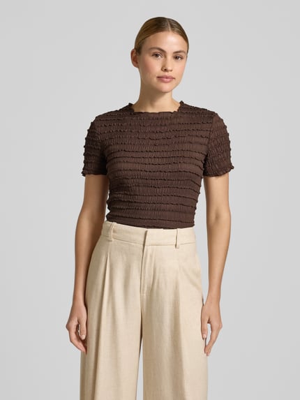 Frauenmodel trägt T-Shirt mit Strukturmuster und Rundhalsausschnitt von Jake*s Collection in Braun, kombiniert mit weiter beige Hose, Slim Fit, Material-Mix mit Stretch-Anteil, Ganzkörperansicht von vorne.