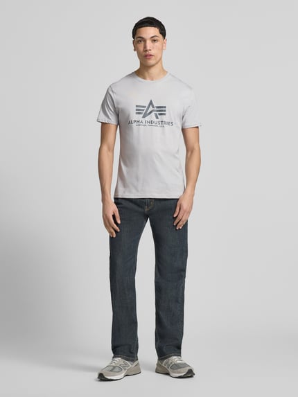 Männermodel trägt Herren T-Shirt mit Label-Detail Modell 'BASIC' von Alpha Industries in Hellgrau, Reine Baumwolle, Gerader-Schnitt, Ganzkörperansicht von vorne.