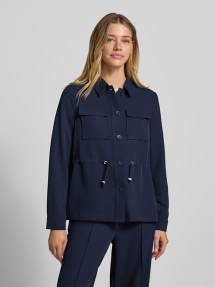 Vrouwenmodel draagt Regular Fit Longblazer mit Brustpattentaschen van s.Oliver BLACK LABEL in effen donkerblauw, lange mouwen, omgeslagen kraag, tunnelkoord in de taille, kleppenzakken op de borst, eenrijige knoopsluiting, longline, gladde textuur, vooraanzicht buste-close-up.