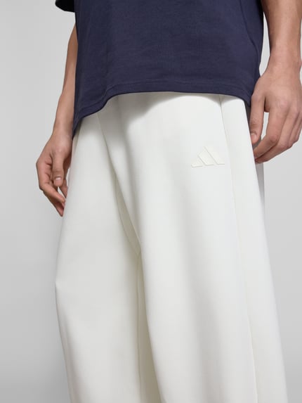 Mężczyznamodel nosi Regular Fit Sweatpants mit Modal-Baumwoll-Anteil von adidas Sportswear, gładki materiał, logo, krój regular fit, elastyczny pas i nogawki, kieszenie boczne, mieszanka modalu i bawełny, zbliżenie na górną część ciała.